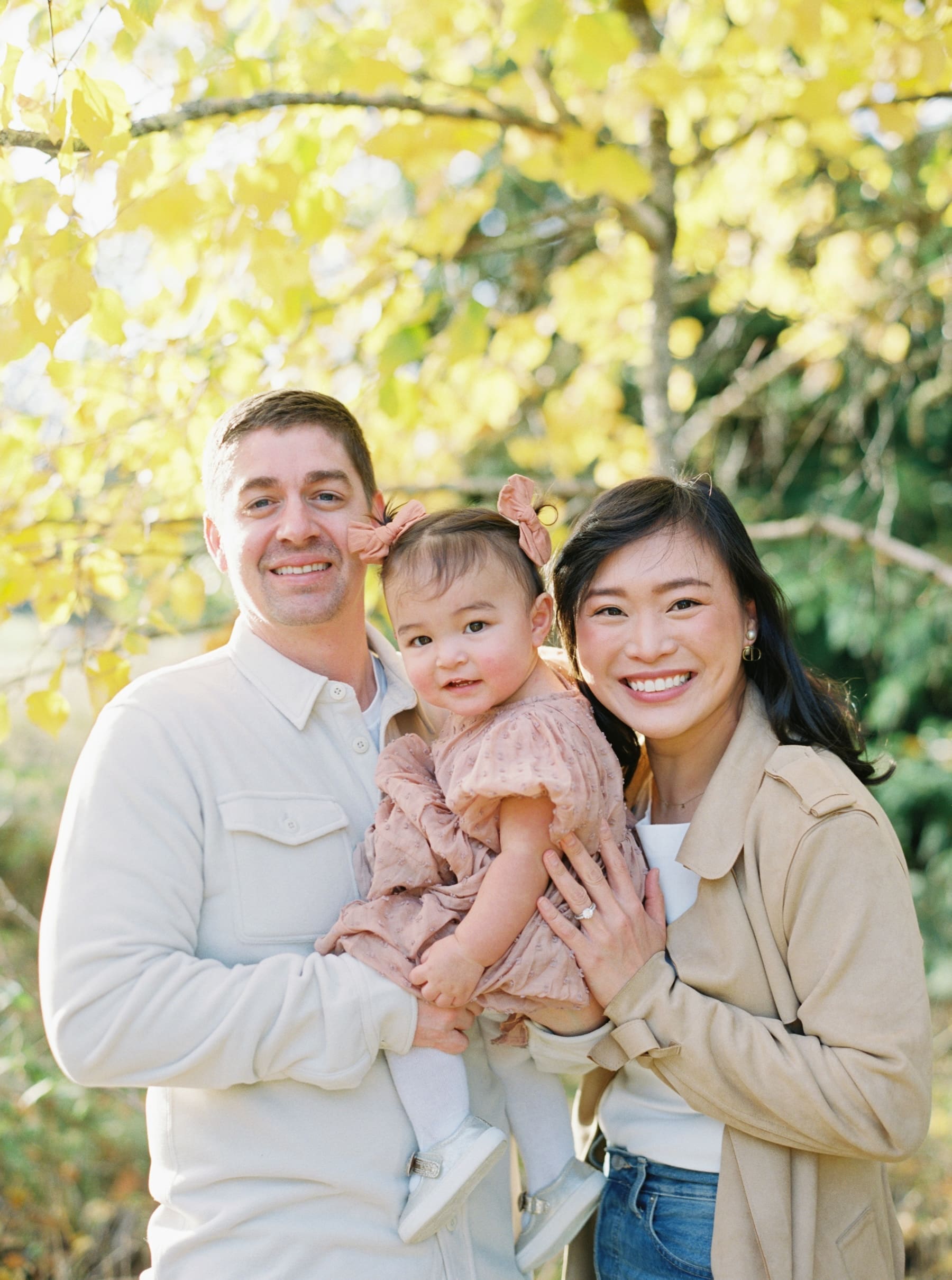 Kirkland family photography at Juanita Bay Park: A happy family of three smiling in front of a tree with yellow leaves.