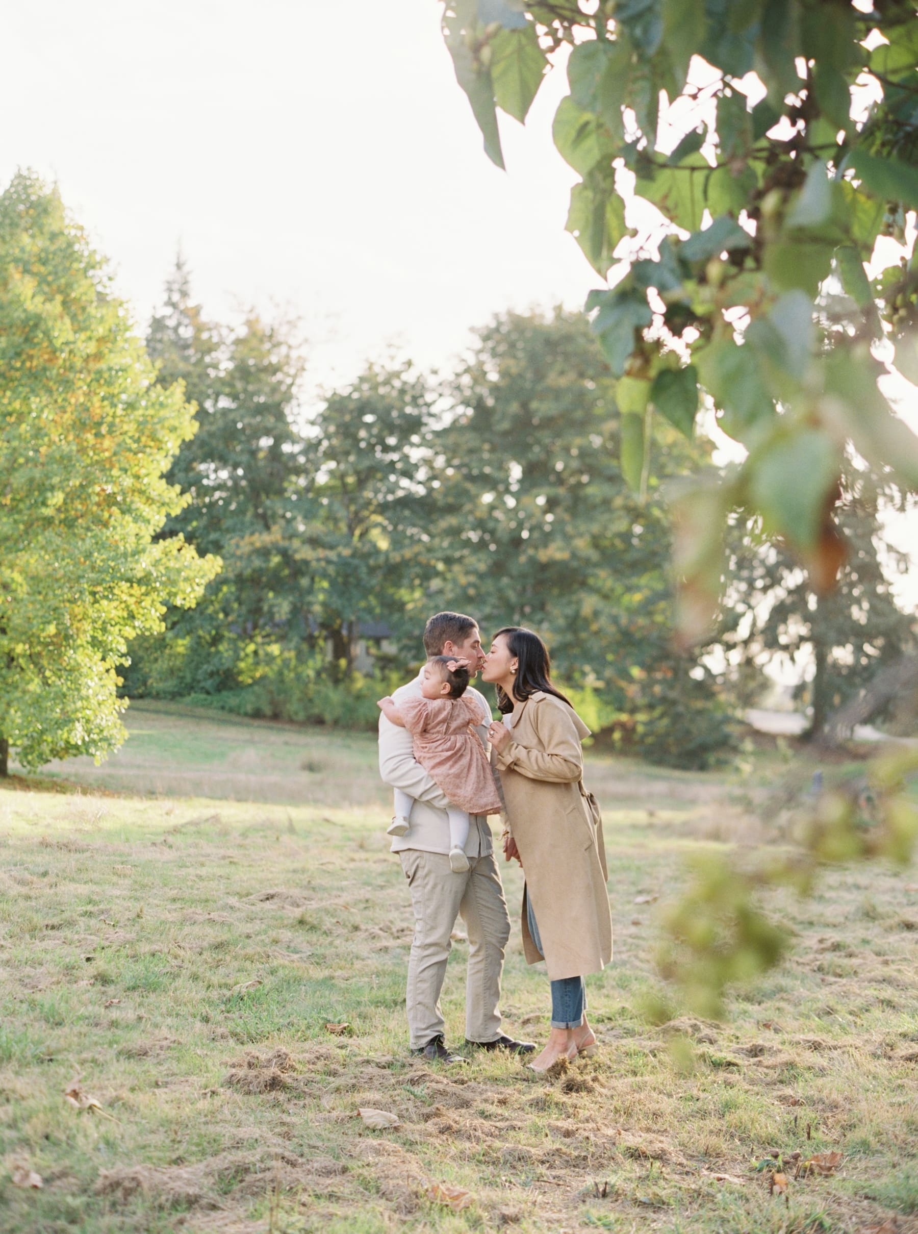 Kirkland family photography session at Juanita Bay Park. Parents kissing while holding their baby girl.