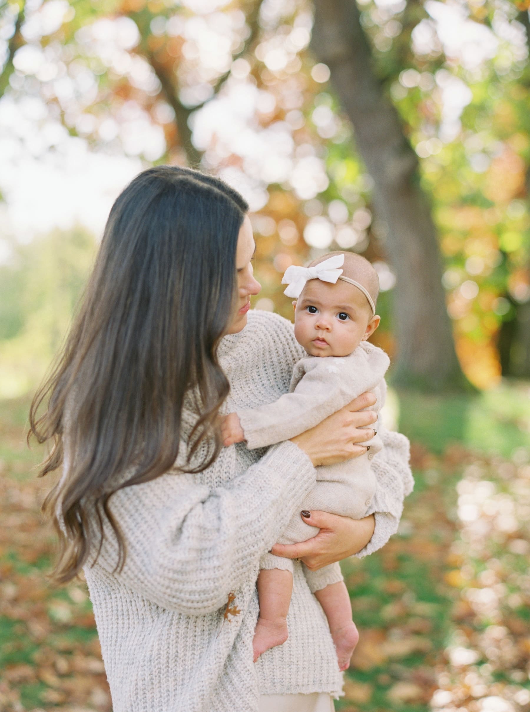 Long haired mother holds cute baby girl with fall foliage surrounding them at Greenlake Park in Seattle