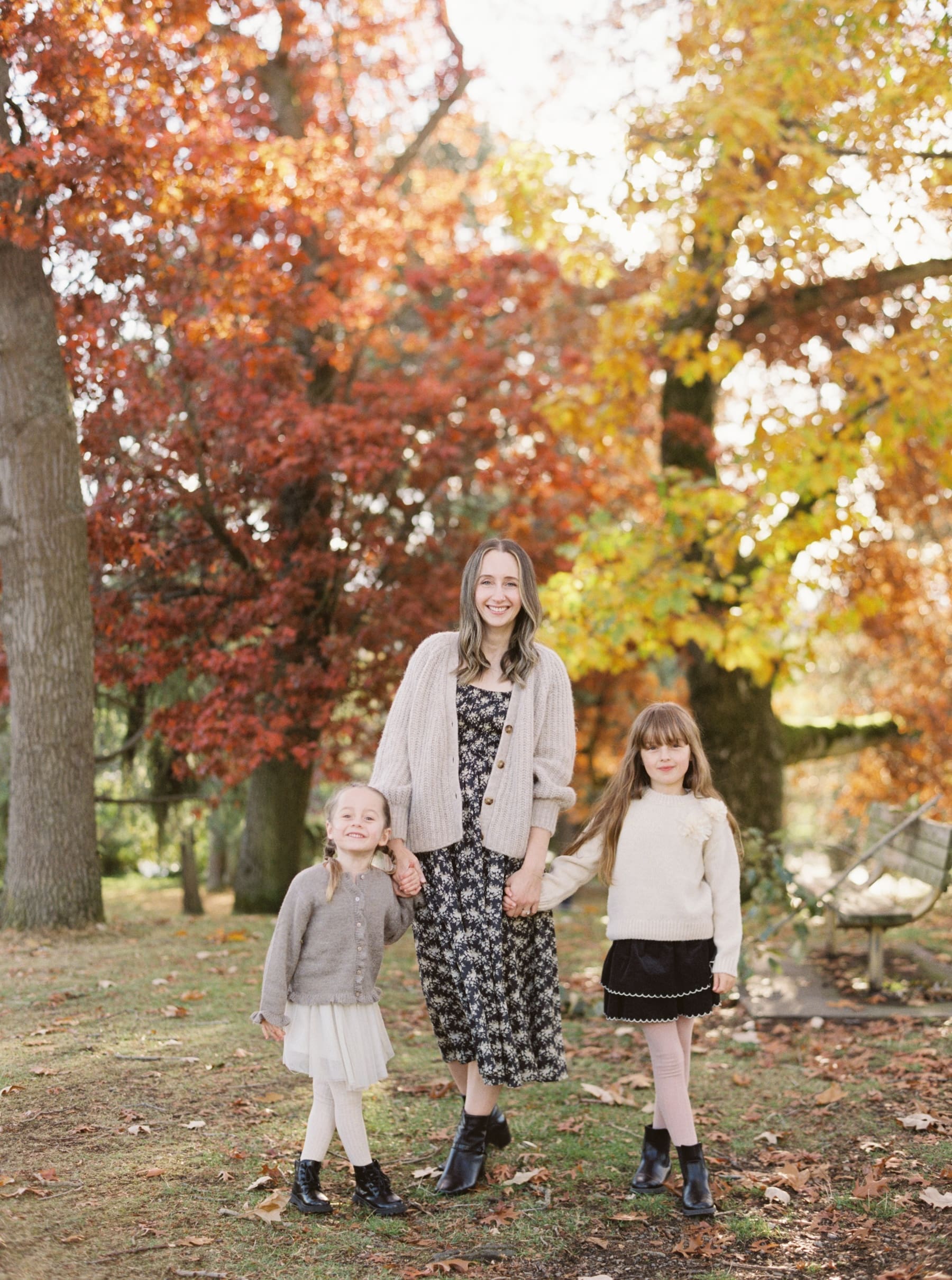 mother poses holding hands with two daughters for family photos in colorful foliage at Greenalake park in Seattle