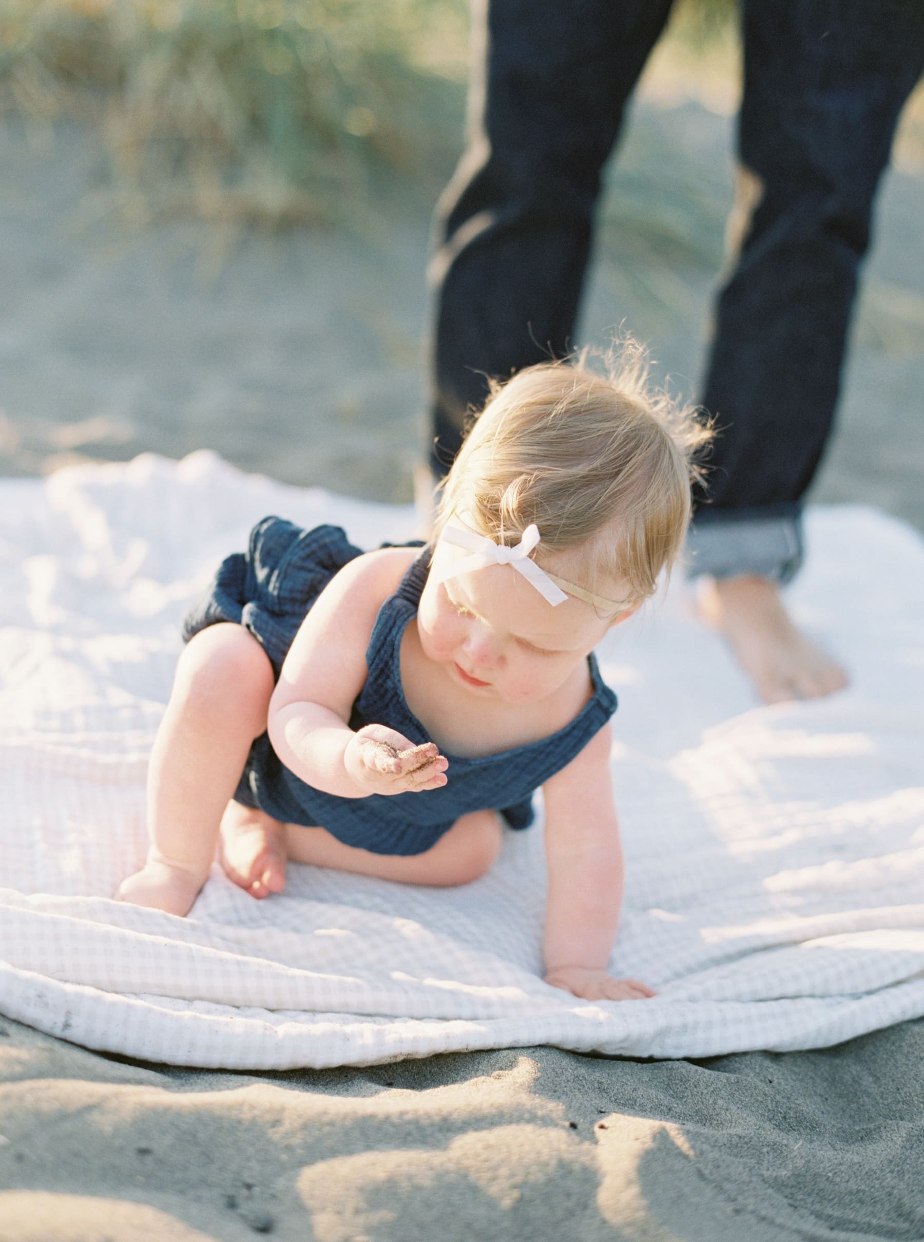 one year old baby girl on beach looking at sand in hand