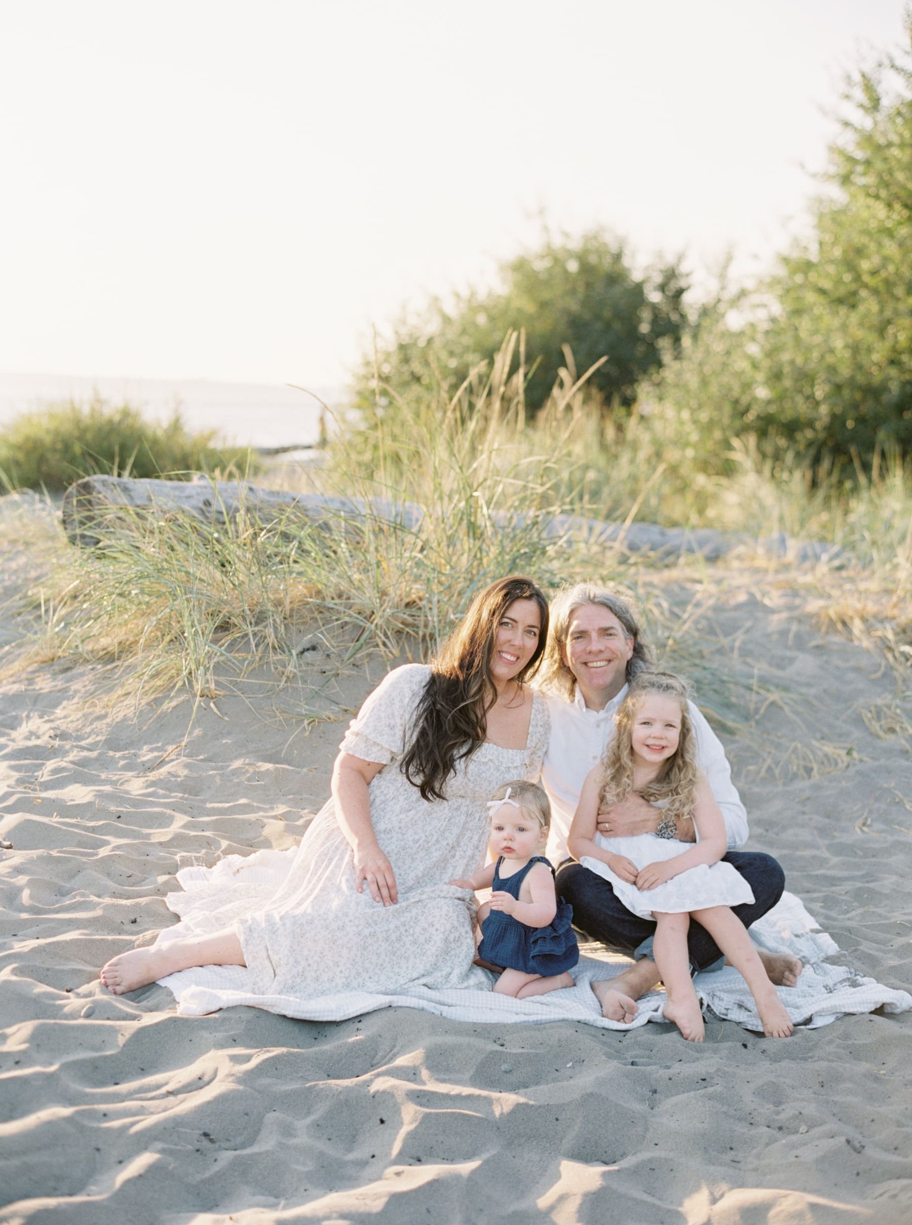 family of four sitting on blanket on sand at beach in seattle for family photos