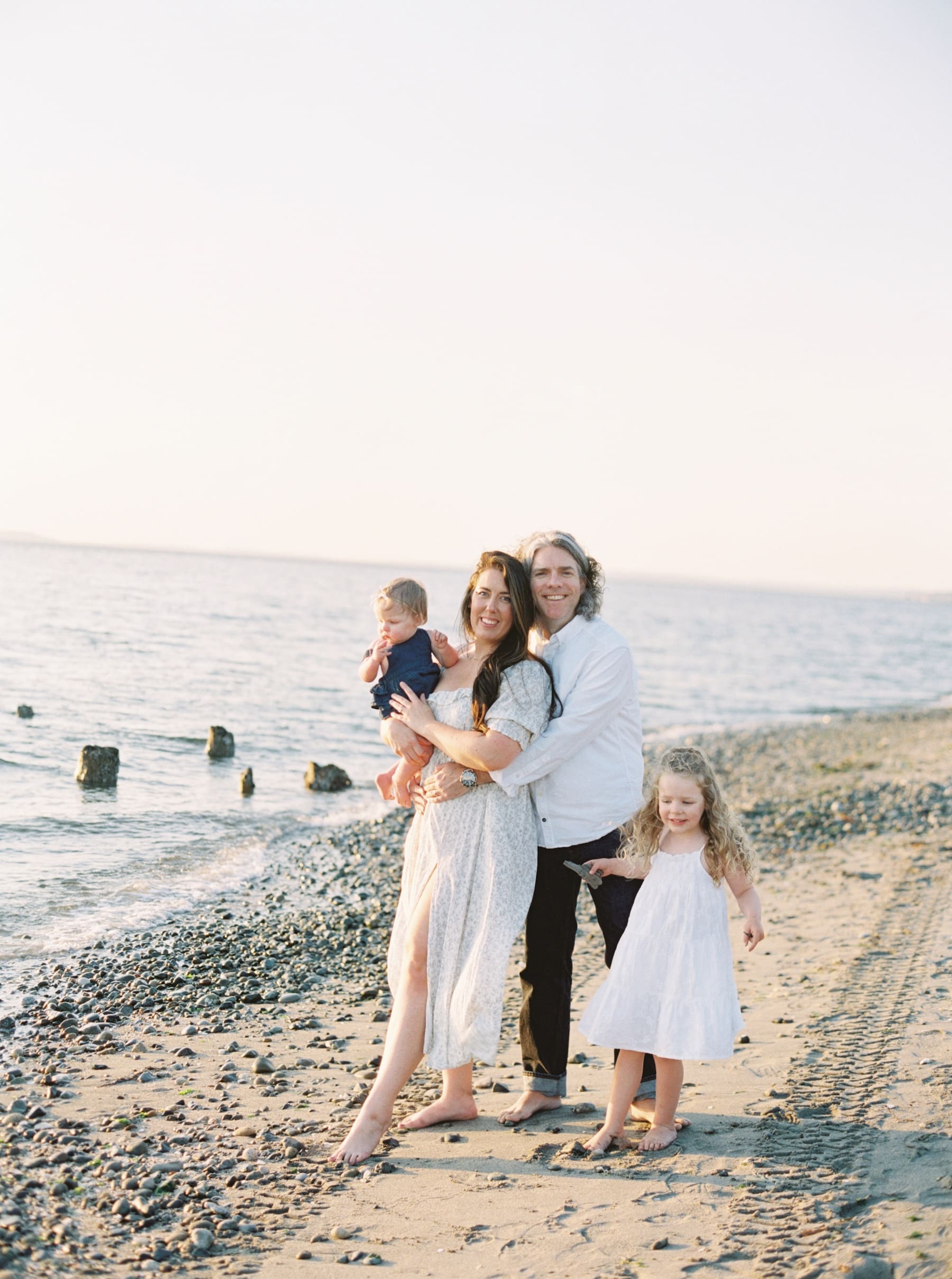 family of four posing for family photos at golden gardens beach in seattle