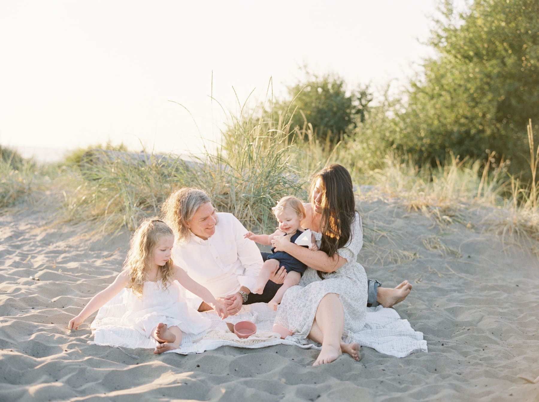 family of four sitting on beach blanket together interacting with each other
