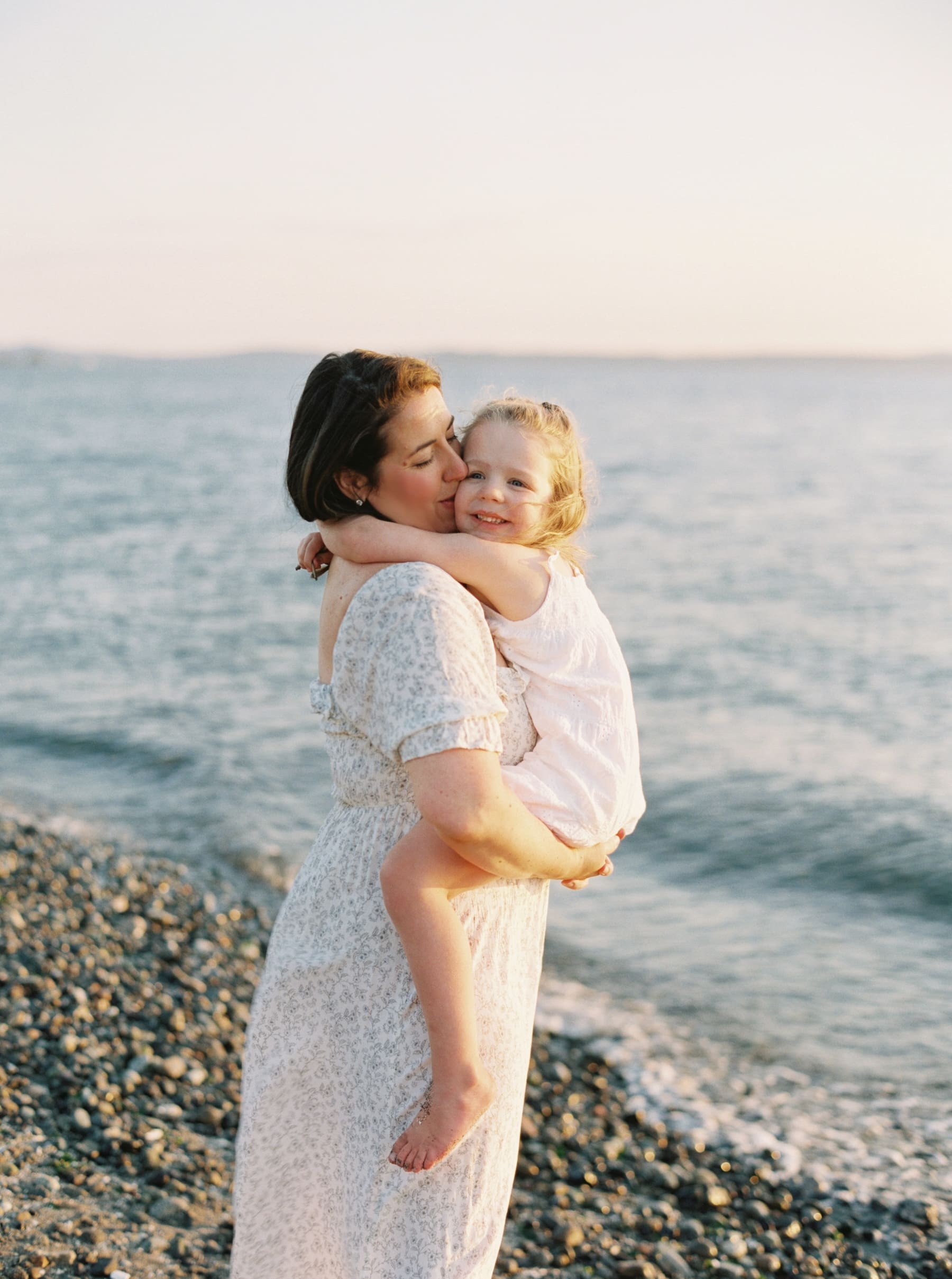 mom holding daughter and kissing her cheek at the beach