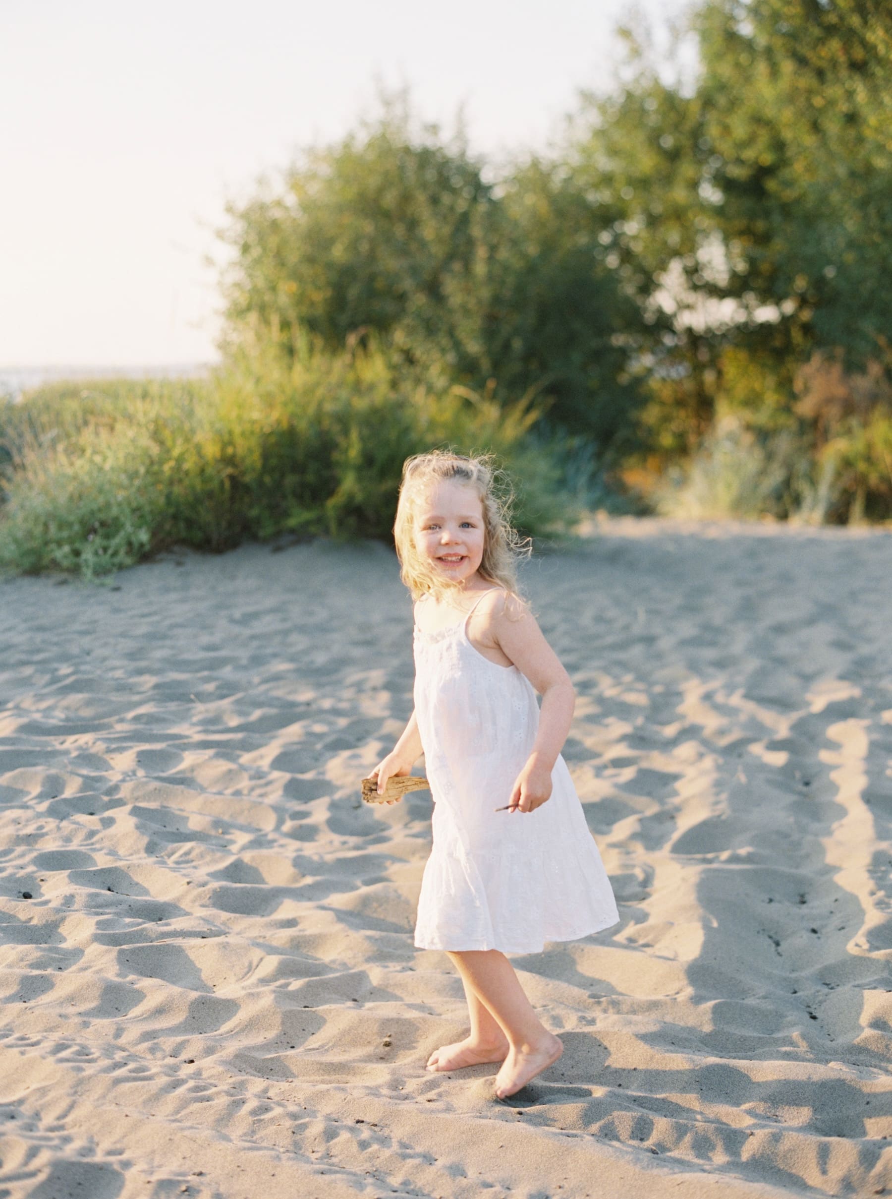 little girl running on sandy beach in white dress in seattle at golden gardens