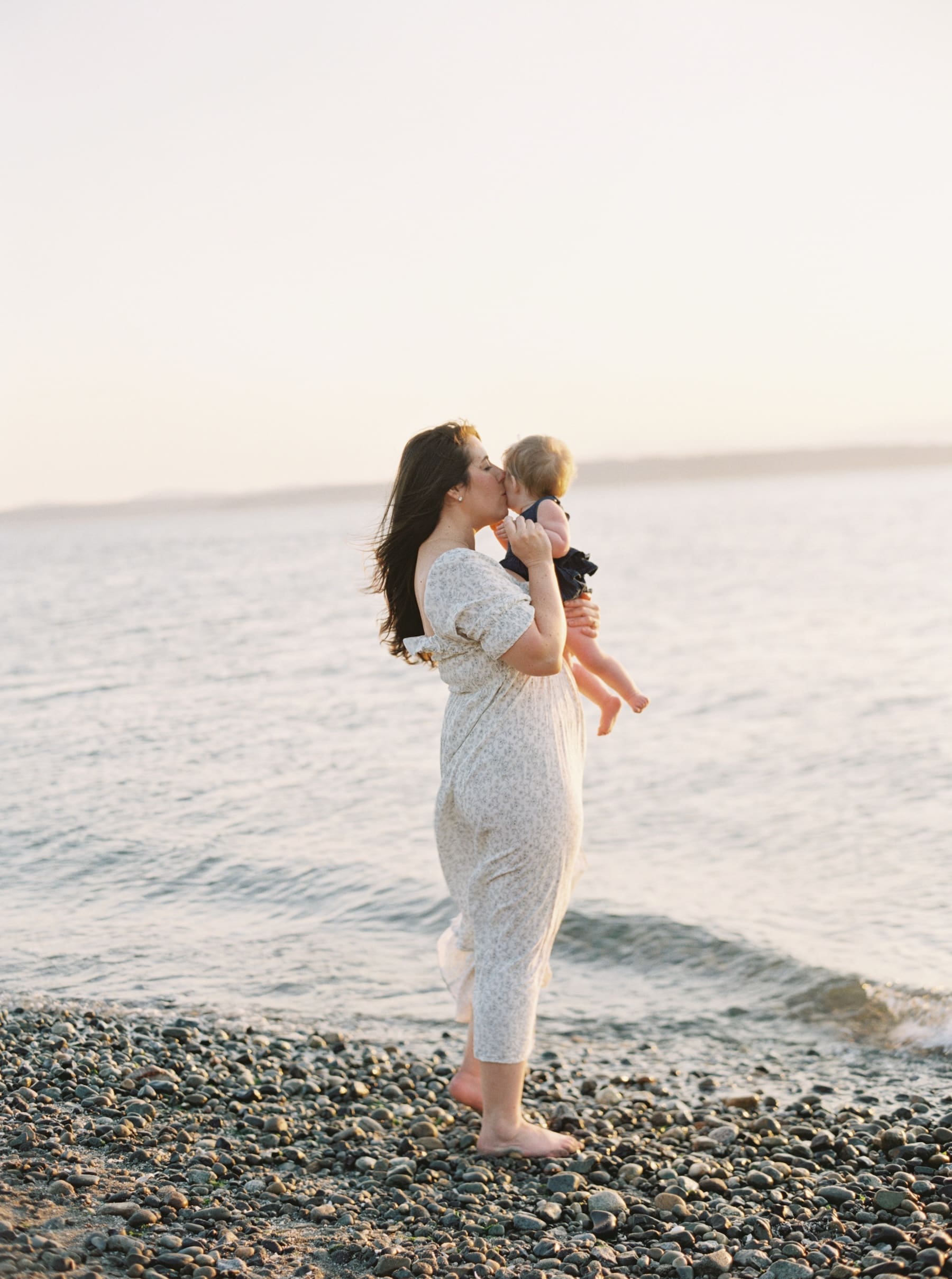 mom holding tiny baby at the waters edge at sunset on the beach