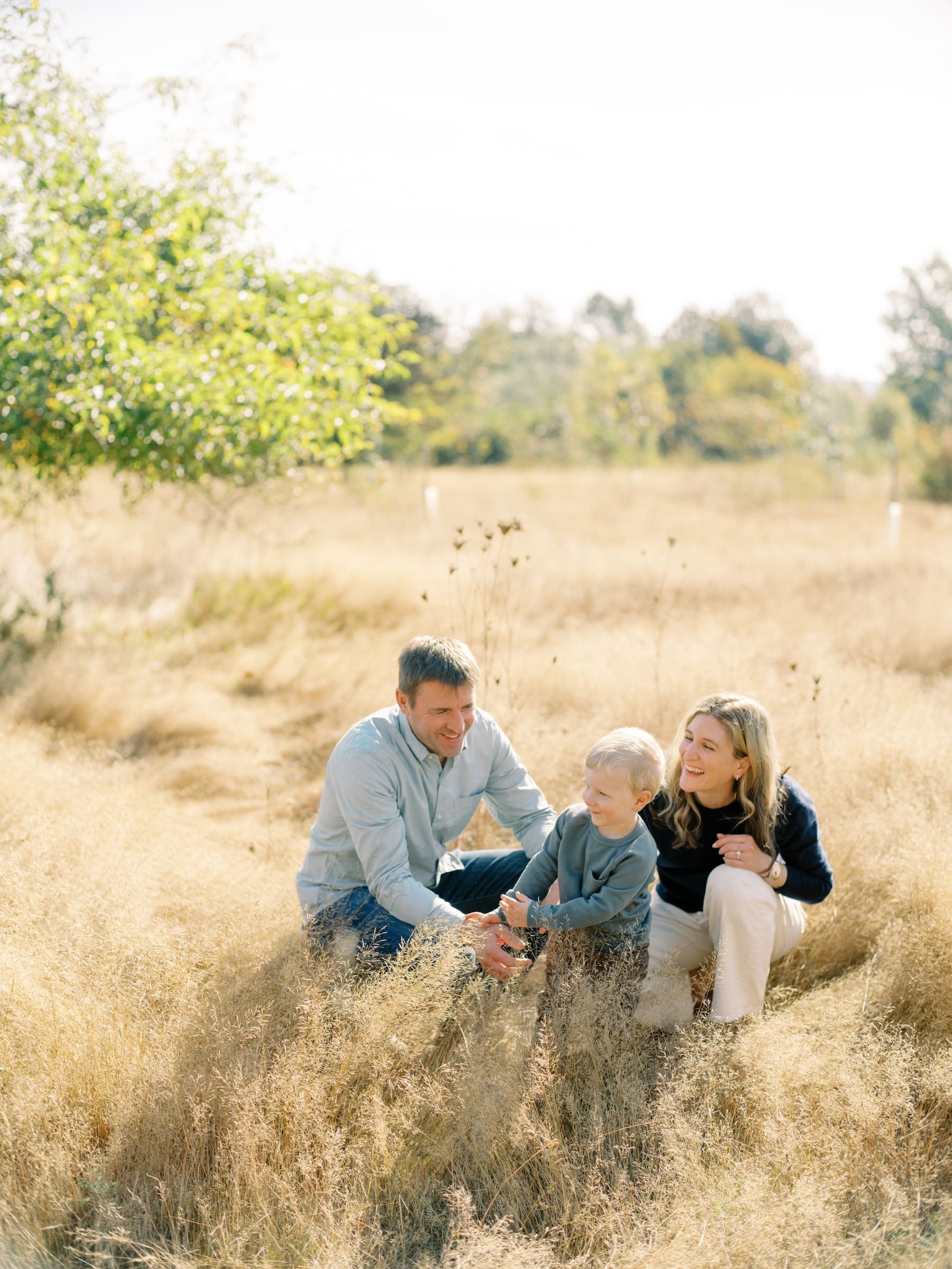 Seattle Fall Mini Session: Family portrait in golden field. Parents with young child smiling, enjoying outdoor photography.
