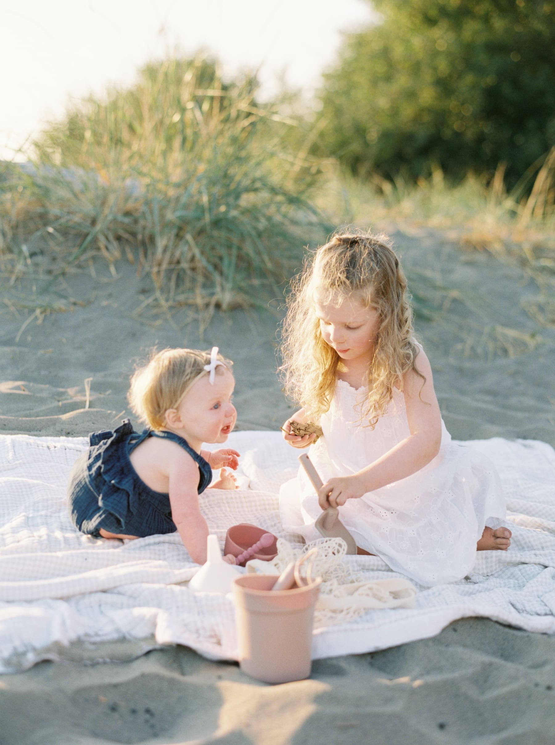 little girl and her baby sister playing in sand at Seattle Golden Garden beach at golden hour