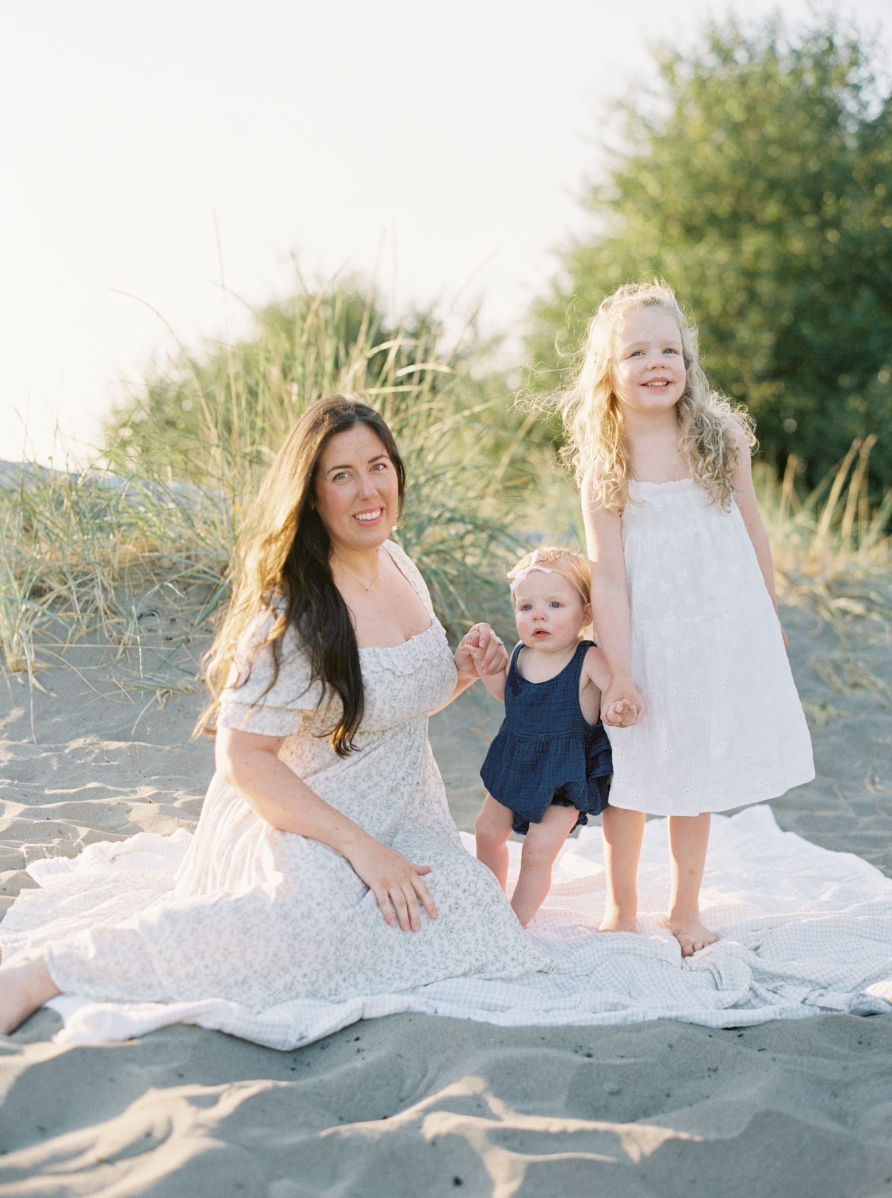 mom smiling at camera with two daughters all in white beach dresses
