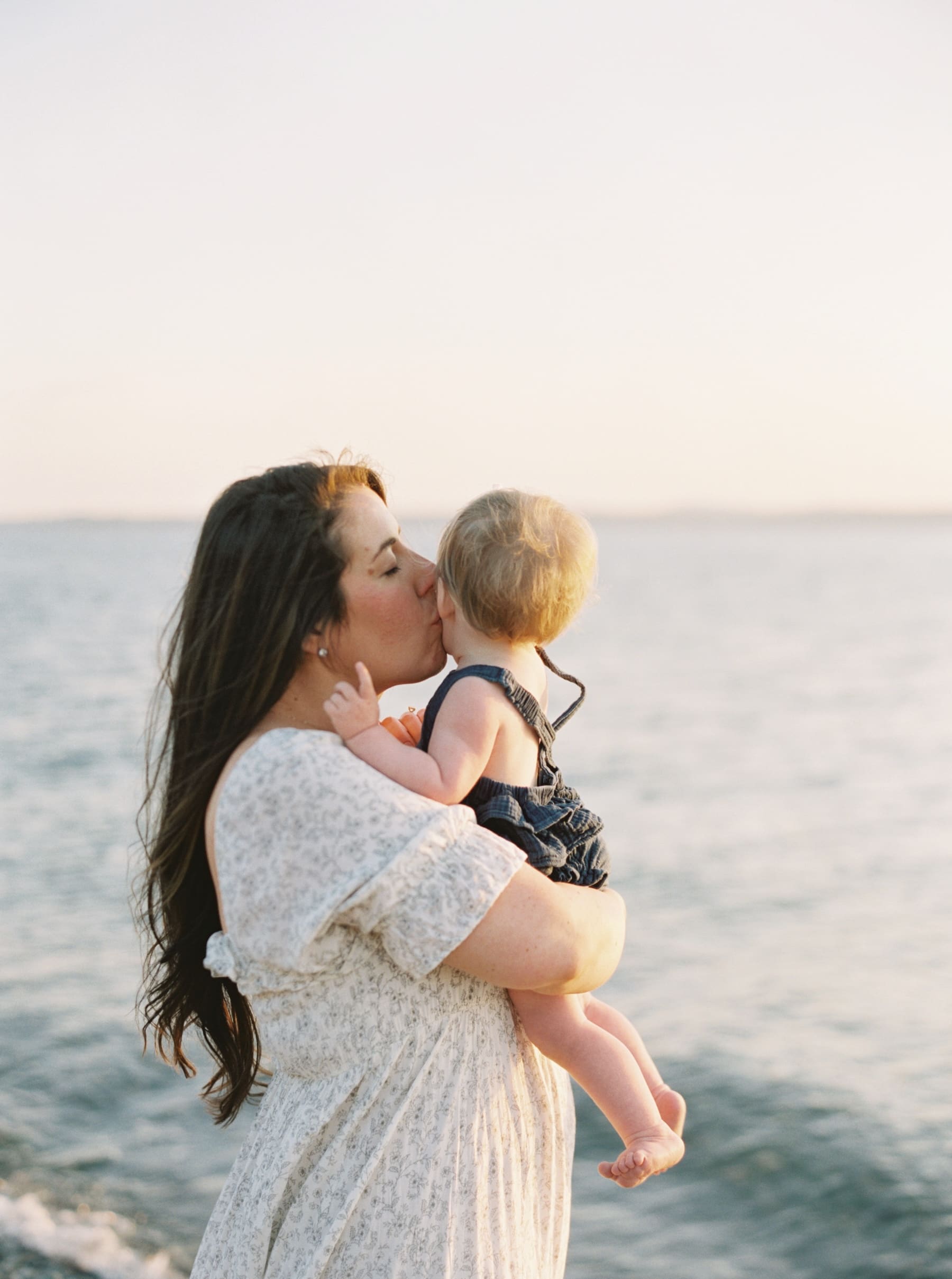 mom kissing baby girls cheek at beach sunset time