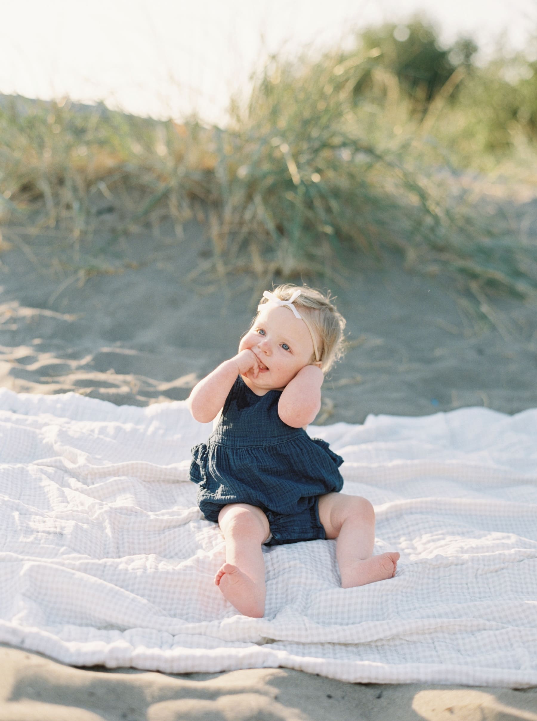 one year old baby girl in navy blue romper sitting on beach blanker