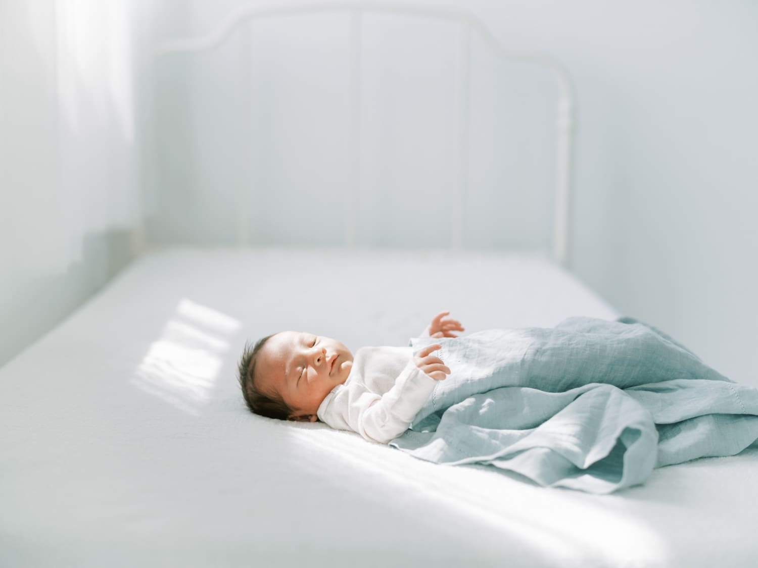 Precious newborn baby Marshall sleeping peacefully on a white bed with a soft blue blanket in natural light.