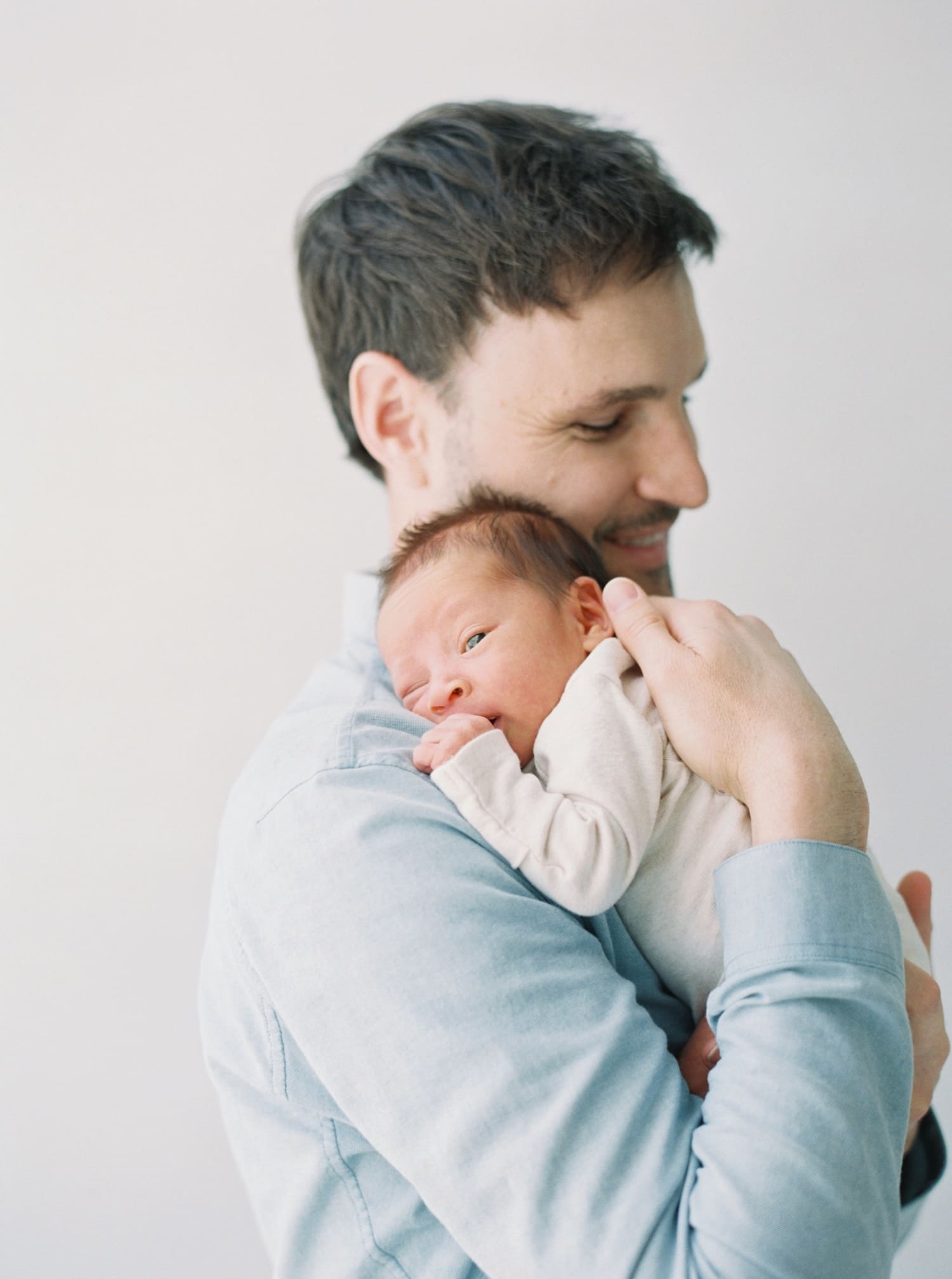 Newborn Marshall held lovingly by his father, soft natural light, tender moment.
