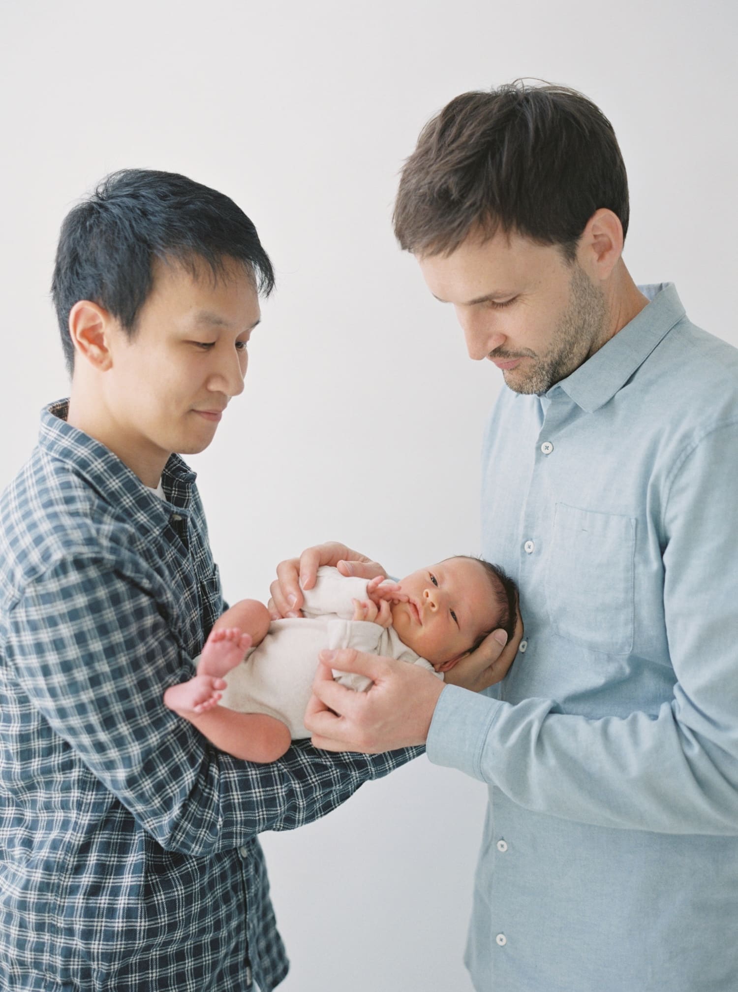 Two fathers lovingly holding their newborn baby, gazing with affection. Newborn family portrait.
