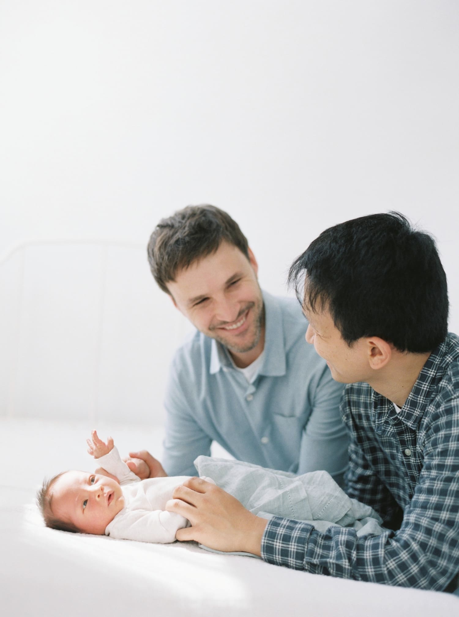 two dads smiling looking over their newborn baby