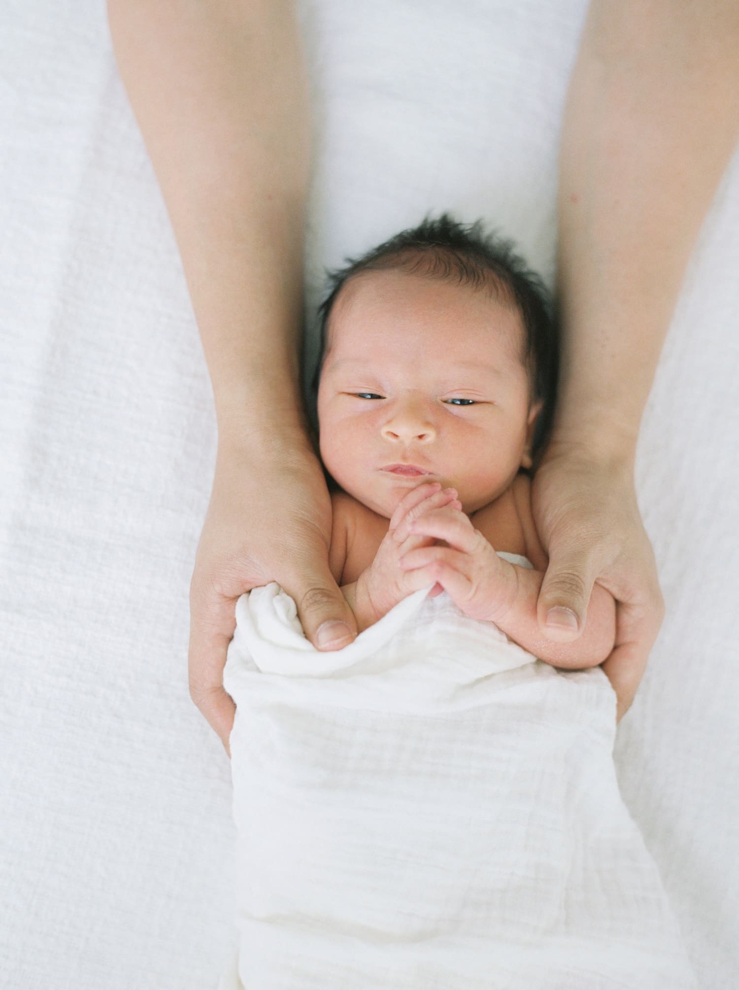 newborn baby boy with hands together and fathers arms wrapped around him